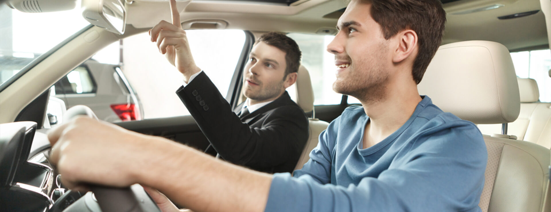 Two men sitting in a car inside a dealer's showroom.